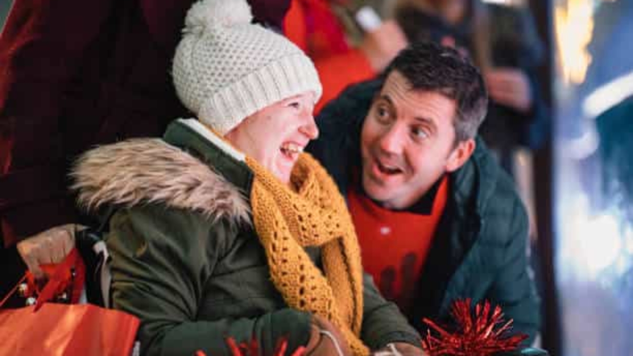 A side-view shot of a father and daughter looking at Christmas decorations on a city street, they are wearing warm Christmas​ clothing.